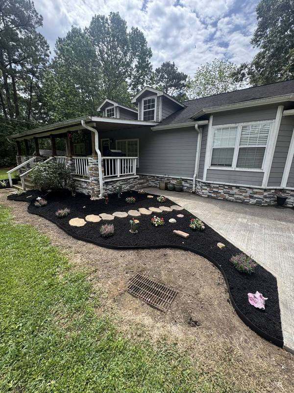 Mulch bed with flowers and stepping stones at a gray home