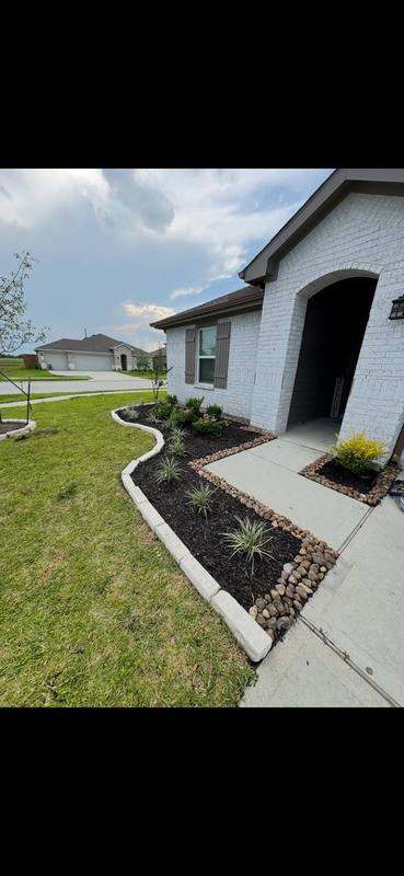 Curbed mulch and river-rock beds along a white brick home's walkway