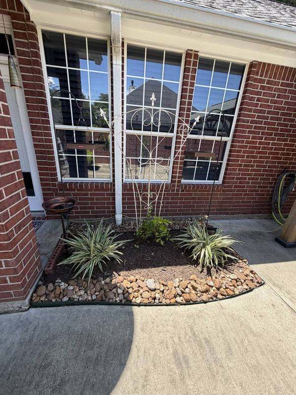 Foundation bed with variegated plants, river rock, and an iron trellis